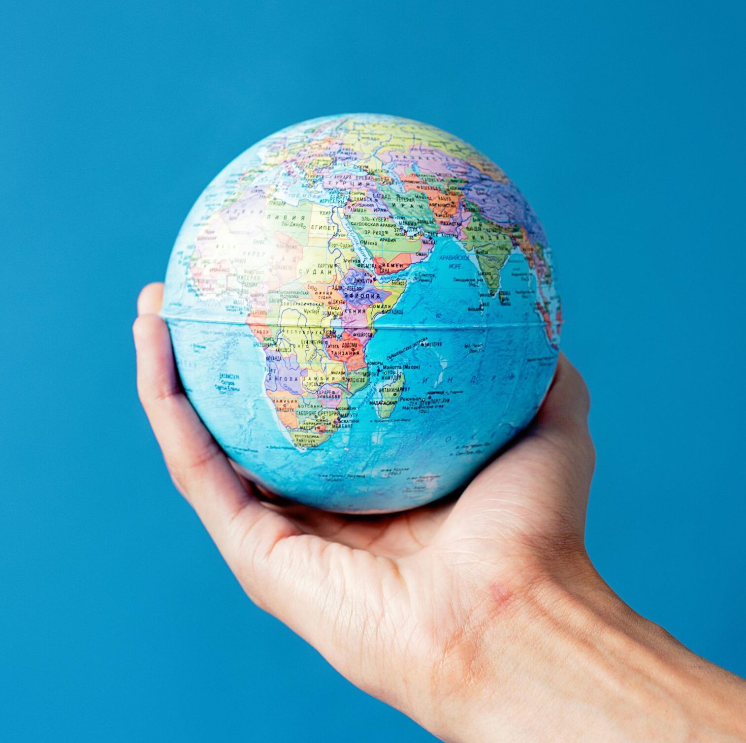 A hand carefully holds a labeled globe against a vibrant blue background, symbolizing world unity.